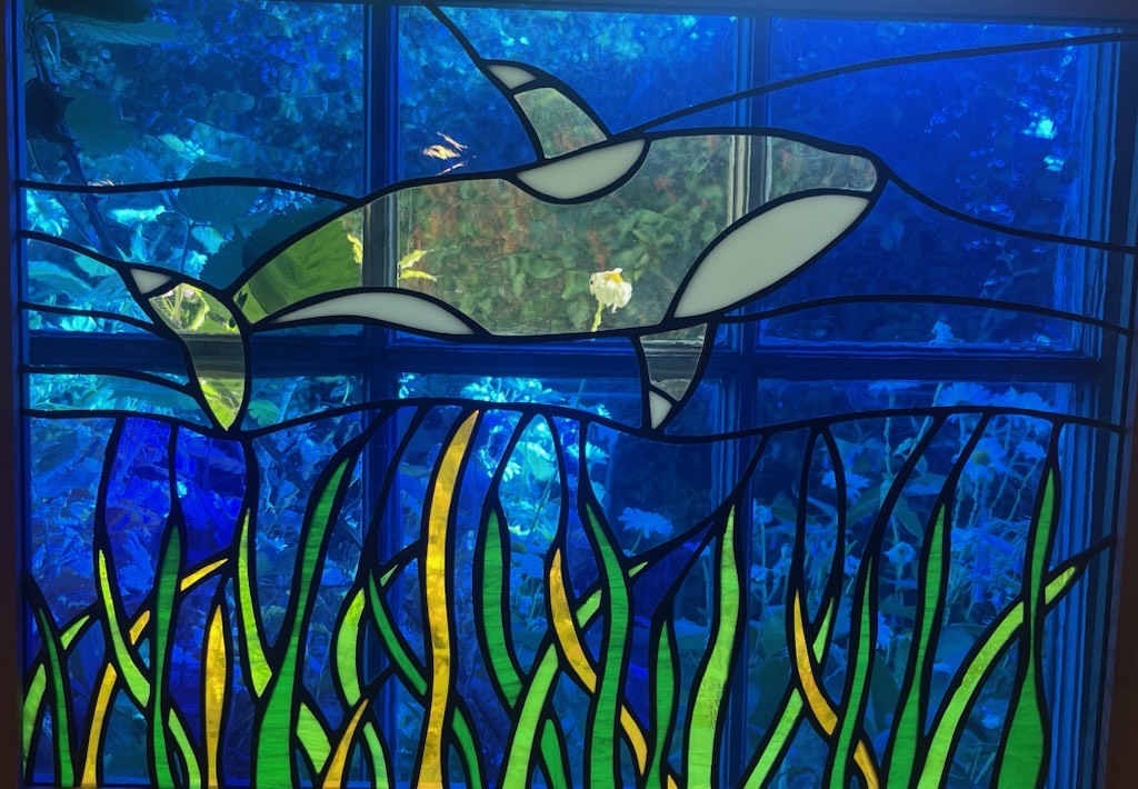 Stained-glass orca swimming above green and yellow kelp